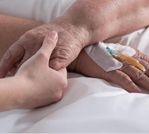 A hand lovingly holding the hand of a patient laying in a hospital bed