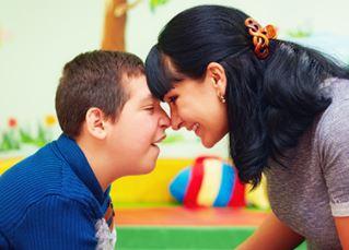 A child and a care provider smiling while leaning on each others foreheads