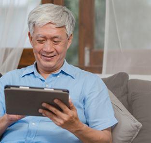 An elderly gentlemen looking at a tablet and smiling
