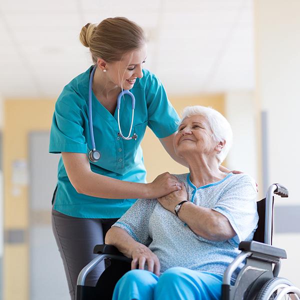 Senior patient in a wheelchair looking up at caregiver with a smile