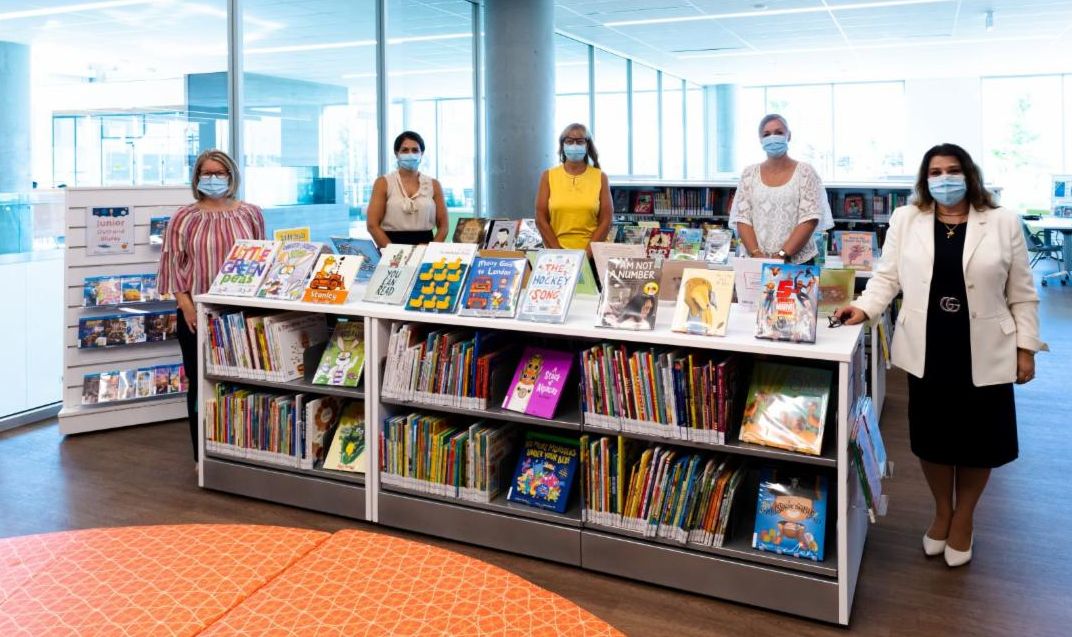 Library shelves with books and staff standing around the shelves masked