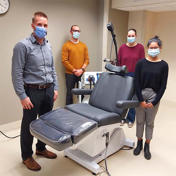 Four masked staff in a clinical room standing around a treatment chair