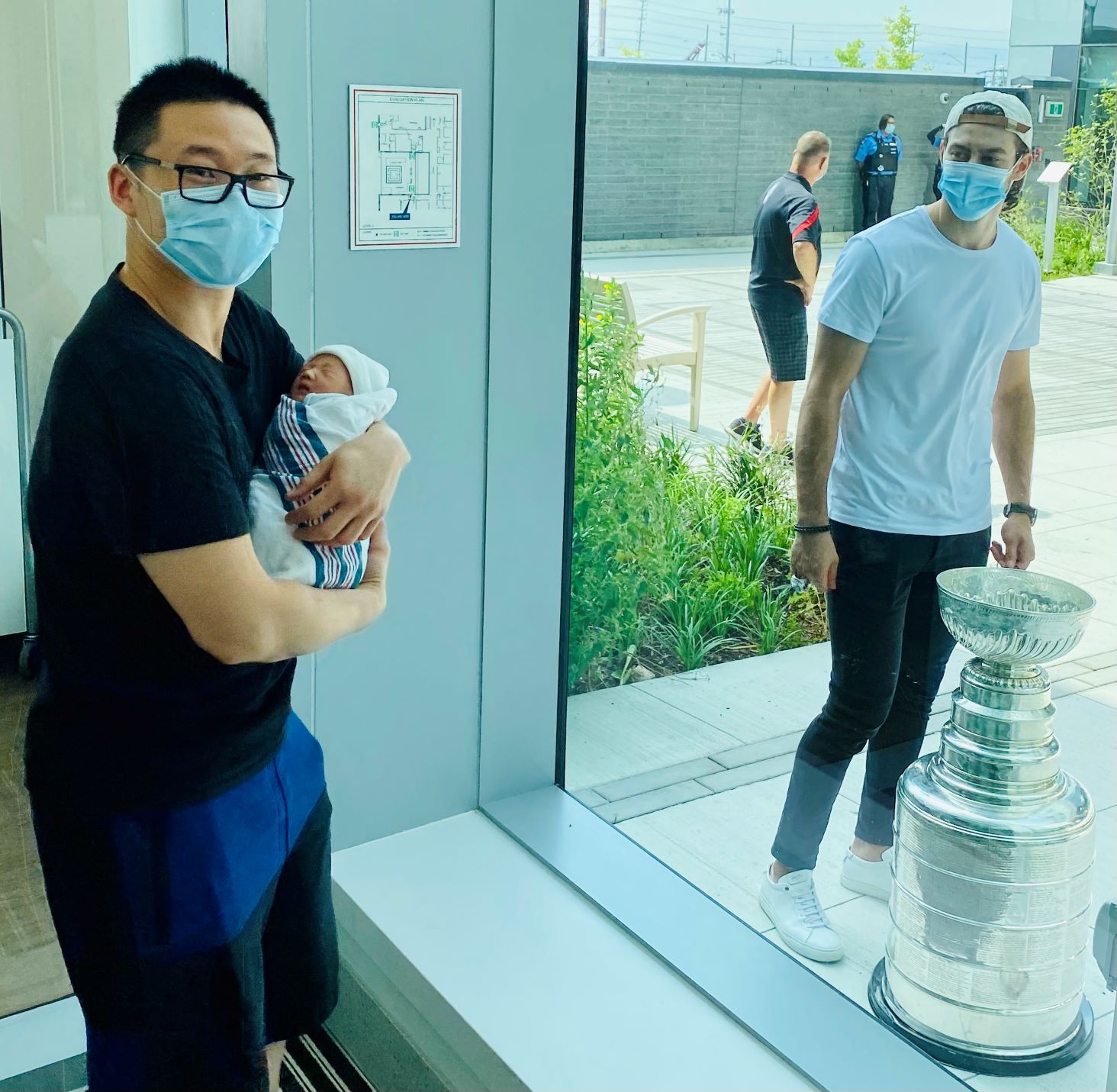 New dad holding baby on inside of window and looking at the Stanley Cup
