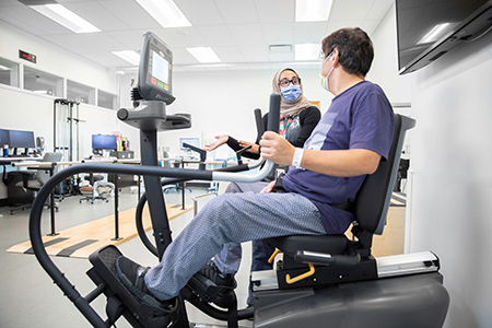 Caregiver speaking to a patient working out on gym equipment