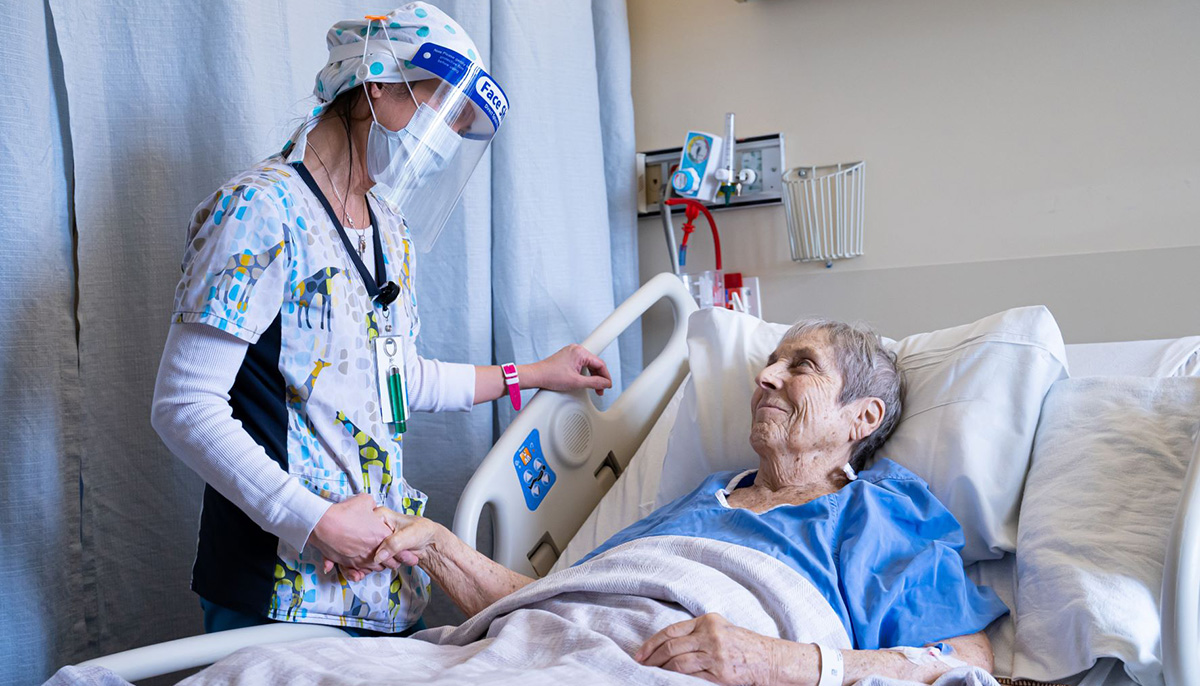 Caregiver at the bedside holding a patient's hand