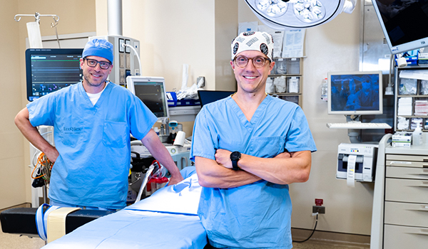 Dr. Michael Kogon and Dr. Ryan Fitzpatrick in scrubs and standing in an OR