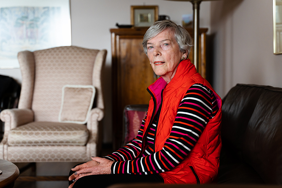 Eleanor dressed in a red vest, sitting on a sofa at her home