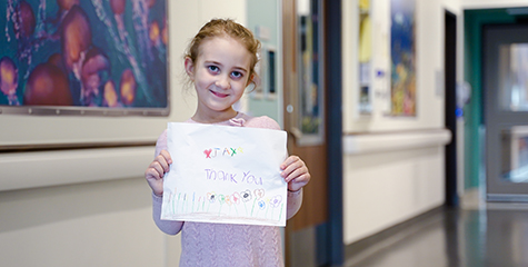 Jax standing in a hospital hall, smiling and holding up a hand-drawn thank you sign